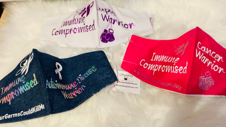 May include: Four fabric face masks with different designs and messages. The masks are white, denim, pink, and white. The messages on the masks include "Immune Compromised", "Cancer Warrior", "Autoimmune Disease Warrior", and "Immune Compromised".