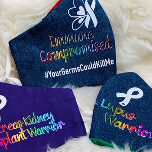 May include: Three denim face masks with white ribbon designs and rainbow text. The top mask reads "Immune Compromised #YourGermsCouldKillMe". The middle mask reads "Pancreas Kidney Transplant Warrior". The bottom mask reads "Lupus Warrior".