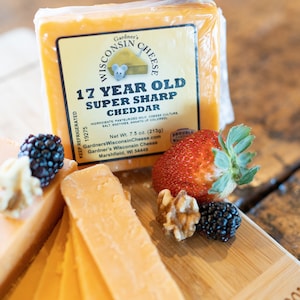 May include: A block of 17 year old Wisconsin Super Sharp Cheddar cheese on a wooden cutting board with strawberries, blackberries, and walnuts. The cheese is wrapped in plastic and has a label that says "Gardner's Wisconsin Cheese".