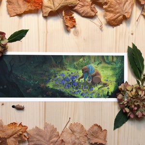 Op de afbeelding: Een bruin dier met een blauwe sjaal plukt paarse bloemen in een bosrijke omgeving. Het dier houdt een mandje in zijn poten. De achtergrond is een donkergroen bos met een lichtgroen grasveld op de voorgrond.