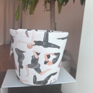 May include: A white ceramic planter with a pattern of black and brown figures in yoga poses.