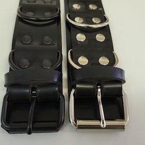 Op de afbeelding: Twee zwarte leren riemen met zilveren gespen en metalen ringen. De riemen hebben rijen zilveren studs.
