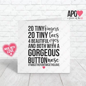 May include: A white greeting card with black text that reads "20 TINY fingers 20 TINY toes 4 BEAUTIFUL eyes AND BOTH WITH A GORGEOUS BUTTON nose #TWICETHEFUNTWICETHELOVE". A pink heart-shaped sticker with "MADE WITH LOVE" is on the left.