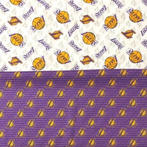 May include: Fabric featuring the Los Angeles Lakers logo and team name. The top half has a white background with repeating logos and basketballs in gold and purple. The bottom half is purple with the team's logo.