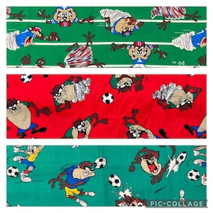 May include: Three different fabric patterns featuring a cartoon Tasmanian Devil playing soccer. The first pattern is green with a white soccer ball and the Tasmanian Devil wearing a blue and white football uniform. The second pattern is red with a white soccer ball and the Tasmanian Devil wearing a red and white soccer uniform. The third pattern is green with a white soccer ball and the Tasmanian Devil wearing a blue and white soccer uniform.