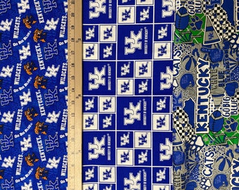 Może przedstawiać: Dwa różne wzory tkanin z logo Wildcats z Uniwersytetu Kentucky. Pierwszy wzór jest niebieski z białymi kwadratami i logo w kolorze białym. Drugi wzór jest biały z różnymi niebieskimi, zielonymi i czarnymi grafikami, w tym logo Wildcats, piłkami do koszykówki i odciskami łap. Tekst "KENTUCKY" jest widoczny w drugim wzorze.