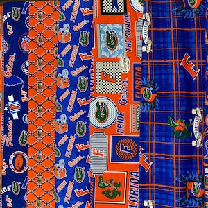 May include: A collection of fabric scraps featuring the University of Florida Gators logo and mascot. The fabrics are in various shades of blue and orange with different patterns, including paisley, plaid, and a repeating alligator design. The text "Florida Gators", "The Swamp", and "Pride Gators" is visible on the fabrics.
