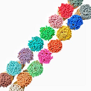 May include: A collection of colorful matchsticks arranged in a diagonal line. The matchsticks are bundled together and have round, colorful heads. The colors include red, orange, yellow, green, blue, purple, pink, and gray.