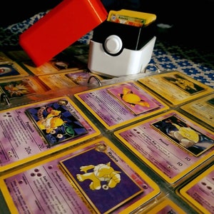 This box contains pokemon cards in a red and white Pokeball style design. This is a storage container for pokemon cards and small valuables.