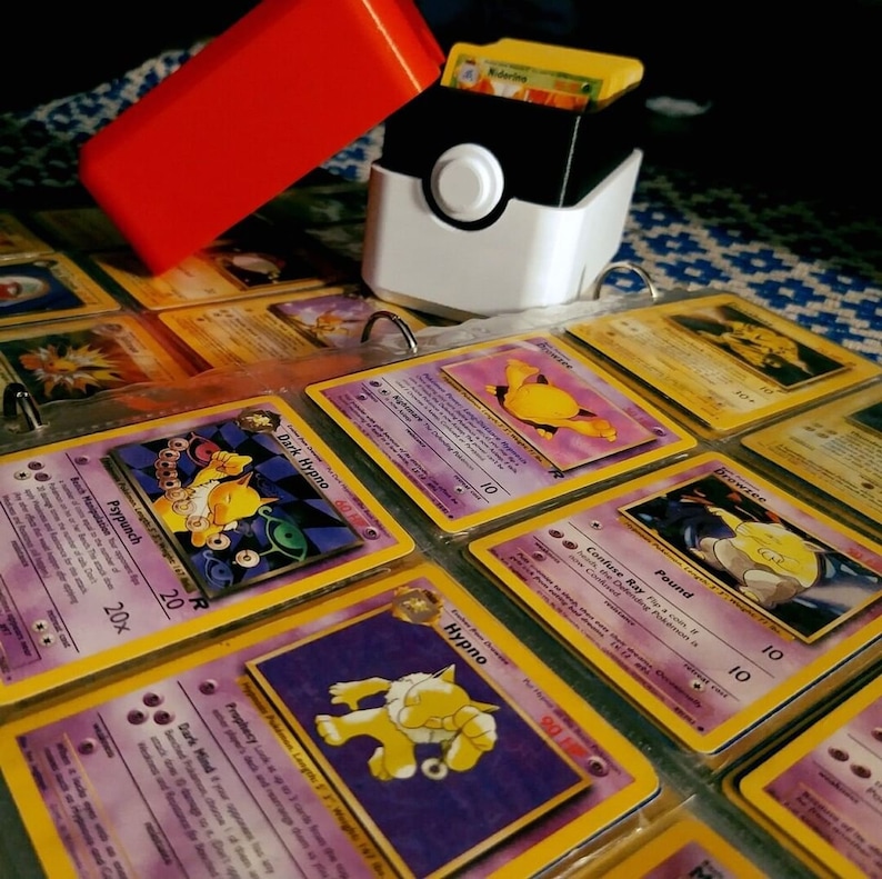 This box contains pokemon cards in a red and white Pokeball style design. This is a storage container for pokemon cards and small valuables.
