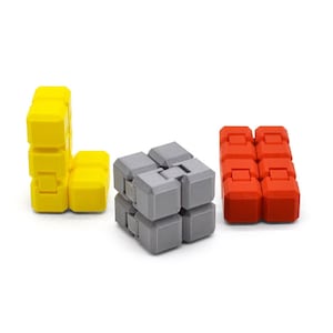 Può includere: Tre piccoli cubi di puzzle interbloccati e colorati. Un cubo è grigio, uno è giallo e l'ultimo è rosso.