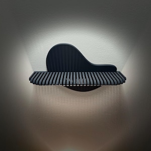 May include: A contemporary wall light in dark grey. The design features a curved top and a slatted, horizontal bottom, creating a soft light on the wall. The fixture's minimalist design is modern and stylish.