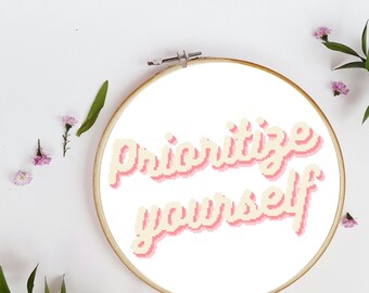 Puede incluir: Un aro de bordado blanco con la frase "prioritize yourself" en letras rosa y amarillo.