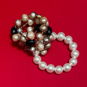 May include: Two pearl necklaces, one with brown and black beads and the other with white beads.