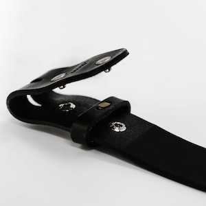 May include: A black leather belt with a metal buckle. The buckle is open and the belt is folded in half.