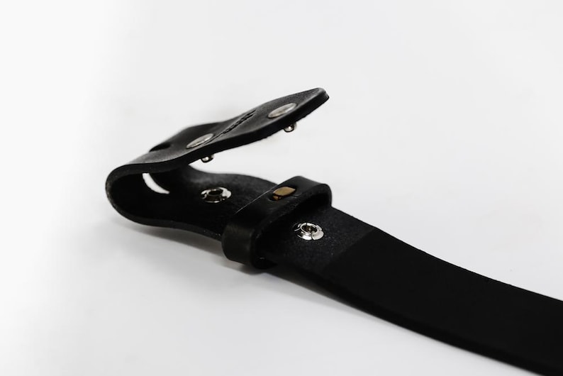 May include: A black leather belt with a metal buckle. The buckle is open and the belt is folded in half.