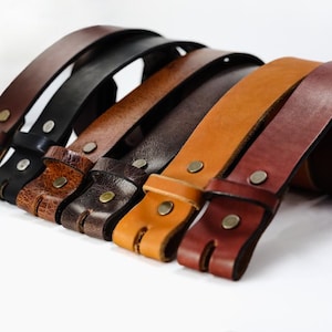 May include: A set of six leather belts in various shades of brown, including black, dark brown, light brown, and tan. The belts are all made of high-quality leather and have a simple, classic design.
