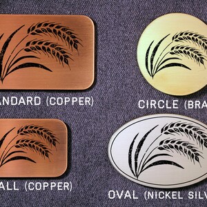 May include: Four metal plaques with a black wheat design. The plaques are in different shapes and sizes: standard, circle, small, and oval. The plaques are made of copper, brass, and nickel silver.