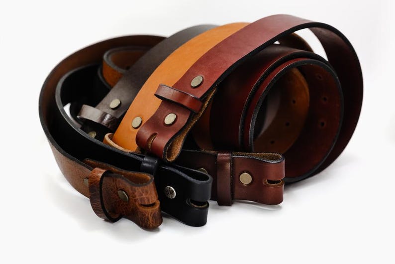 May include: Four leather belts in different shades of brown, with a buckle on each. The belts are stacked on top of each other.