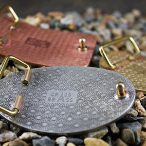 May include: Three metal belt buckles with different finishes. The buckles are round and have a decorative pattern. The buckles are made by "CRASS BRASS".
