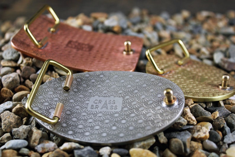 May include: Three metal belt buckles with different finishes. The buckles are round and have a decorative pattern. The buckles are made by "CRASS BRASS".