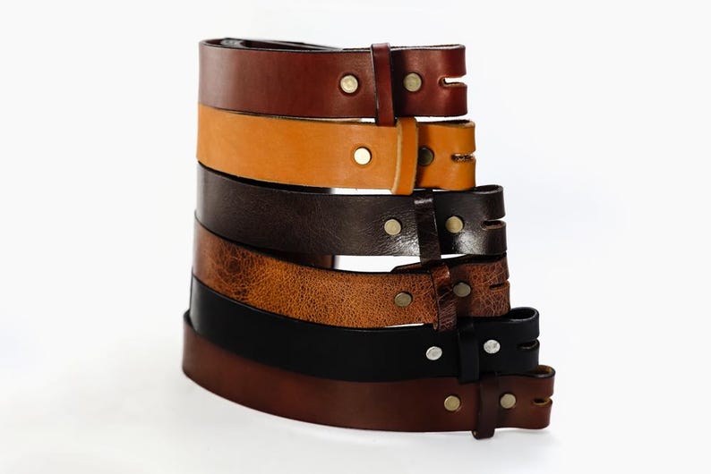May include: A stack of six leather belts in various shades of brown, black, and tan. The belts are all made of leather and have a simple design with a single buckle.