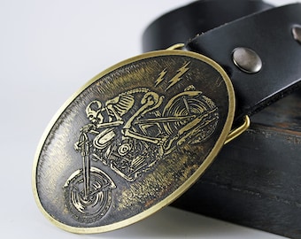 May include: Oval brass belt buckle featuring a skeleton riding a motorcycle with lightning bolts. The buckle is attached to a black leather belt with two silver rivets. The design has a vintage, biker theme.