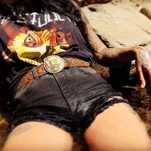 May include: A woman wearing a black tank top with a graphic print of a wolf's head and a brown leather belt with a metal buckle. The belt buckle features a design of a mountain range and the words "National Parks Service".