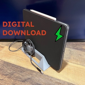 Op de afbeelding: Een zwarte tabletcomputer met een witte stylus en een groene bliksem-sticker staat op een grijze standaard. De tablet is verbonden met een zwarte kabel. De tekst "DIGITAL DOWNLOAD" is zichtbaar in de afbeelding.