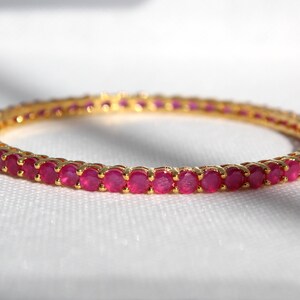 May include: A gold bangle bracelet with a row of pink round stones.