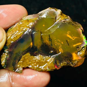 May include: A rough, natural opal gemstone with a yellow, orange, and green iridescent sheen. The opal is set in a matrix of brown rock.