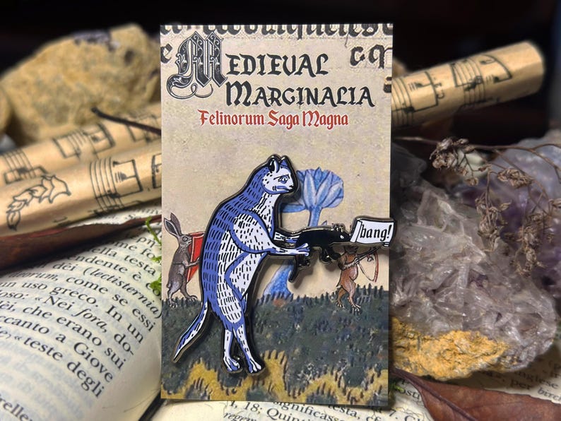 May include: A blue cat holding a gun with a speech bubble that says "bang!" The cat is part of a medieval style illustration with a background of green and brown.