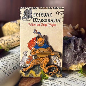 May include: A colorful enamel pin featuring a cat playing a lute. The cat is wearing a blue and white robe and has a red and orange tail. The pin is set against a background of a medieval-style illustration with the text "Medieval Marginalia Felinorum Saga Magna".