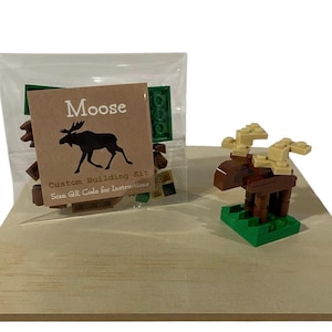 May include: A custom building kit for a moose, with a completed moose model and a bag of building blocks. The model is brown and tan, standing on a green base. The kit includes a card with the word "Moose" and a QR code.