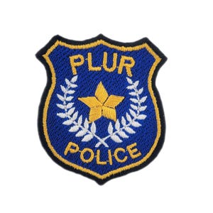 May include: Embroidered patch in a shield shape with the words "PLUR POLICE" in gold lettering. The patch features a gold star and white laurel branches on a blue background, with a gold border.