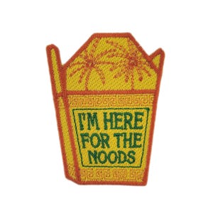 May include: Embroidered patch in the shape of a Chinese takeout container. The patch is yellow with orange trim and features the text "I'M HERE FOR THE NOODS" in green. Two orange palm trees are embroidered on the top.