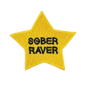 May include: A yellow, star-shaped embroidered patch featuring the text "SOBER RAVER" in black. The patch has a textured surface, suggesting it's designed to be sewn or ironed onto fabric items like jackets or bags.