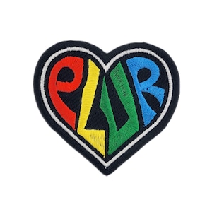 May include: Heart-shaped embroidered patch with the letters "ELVR" in red, yellow, green, and blue. The patch has a black background and a white border, suitable for clothing or accessories.