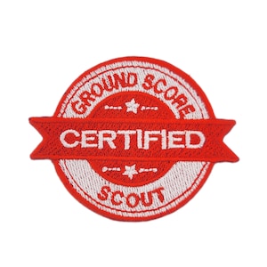 May include: A red and white embroidered patch. The patch features the words "GROUND SCORE CERTIFIED SCOUT" in white lettering. The design is circular with a red banner across the centre, and includes stars and dashes.