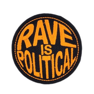 May include: Circular embroidered patch featuring the words "RAVE IS POLITICAL" in orange stitching on a black background. The patch has an orange border. The design is striking and clear.