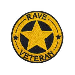 May include: Circular embroidered patch featuring a yellow star on a black base, framed by a yellow border. The words "RAVE" and "VETERAN" are stitched in yellow. The patch is set against a white background.