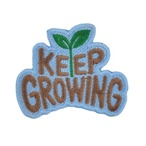 May include: Embroidered patch with the words "KEEP GROWING" in brown thread on a light blue background. A green sprout is in the center. The patch has a light blue border.
