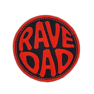 May include: A circular patch featuring the text "RAVE DAD" in bold red lettering. The words are set against a black backdrop, framed by a red stitched edge. This patch is suitable for application on garments or accessories.
