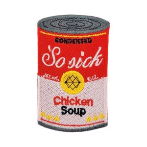 Puede incluir: Parche bordado con forma de lata de sopa de pollo condensada. La lata es roja con las palabras "So sick" en escritura blanca y "Chicken Soup" en negro. Un diseño geométrico amarillo y negro está centrado en la lata.