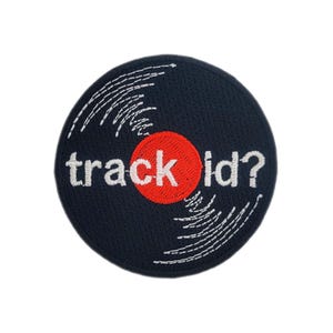May include: A round, navy blue patch with white stitching and the words "track id?" in white text. A red circle is behind the word "track". The patch resembles a vinyl record.