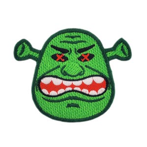 May include: Embroidered patch featuring a green ogre face with an angry expression. The ogre has red crossed-out eyes, a wide open mouth with white teeth, and small, green, ear-like protrusions. The patch is likely for clothing or accessories.
