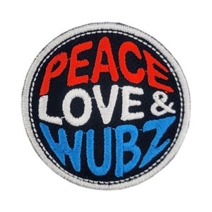 May include: Circular embroidered patch featuring the words "PEACE LOVE & WUBZ" in red, white, and blue. The patch has a black background and a white stitched border. The text is in a bold, playful font.