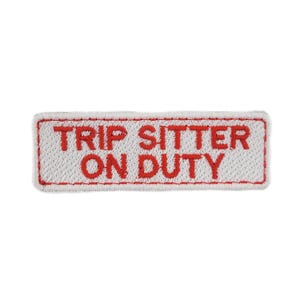 Könnte beinhalten: Ein rechteckiger Aufnäher mit dem roten Schriftzug "TRIP SITTER ON DUTY" auf weißem Grund. Der Aufnäher hat einen roten Rand und ist wahrscheinlich zum Aufnähen auf Kleidung oder Taschen gedacht.