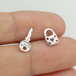 May include: A pair of silver earrings, one shaped like a key and the other shaped like a padlock with a heart cutout.