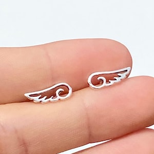 Puede incluir: Un par de pendientes de plata con forma de alas de ángel. Las alas son delicadas y tienen una forma ligeramente curvada.